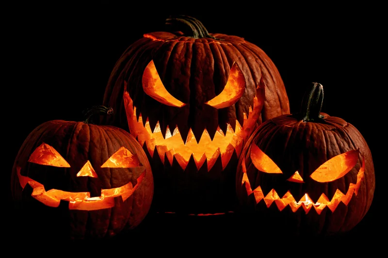 Three carved jack-o-lanterns glowing in the dark with menacing faces arranged closely together