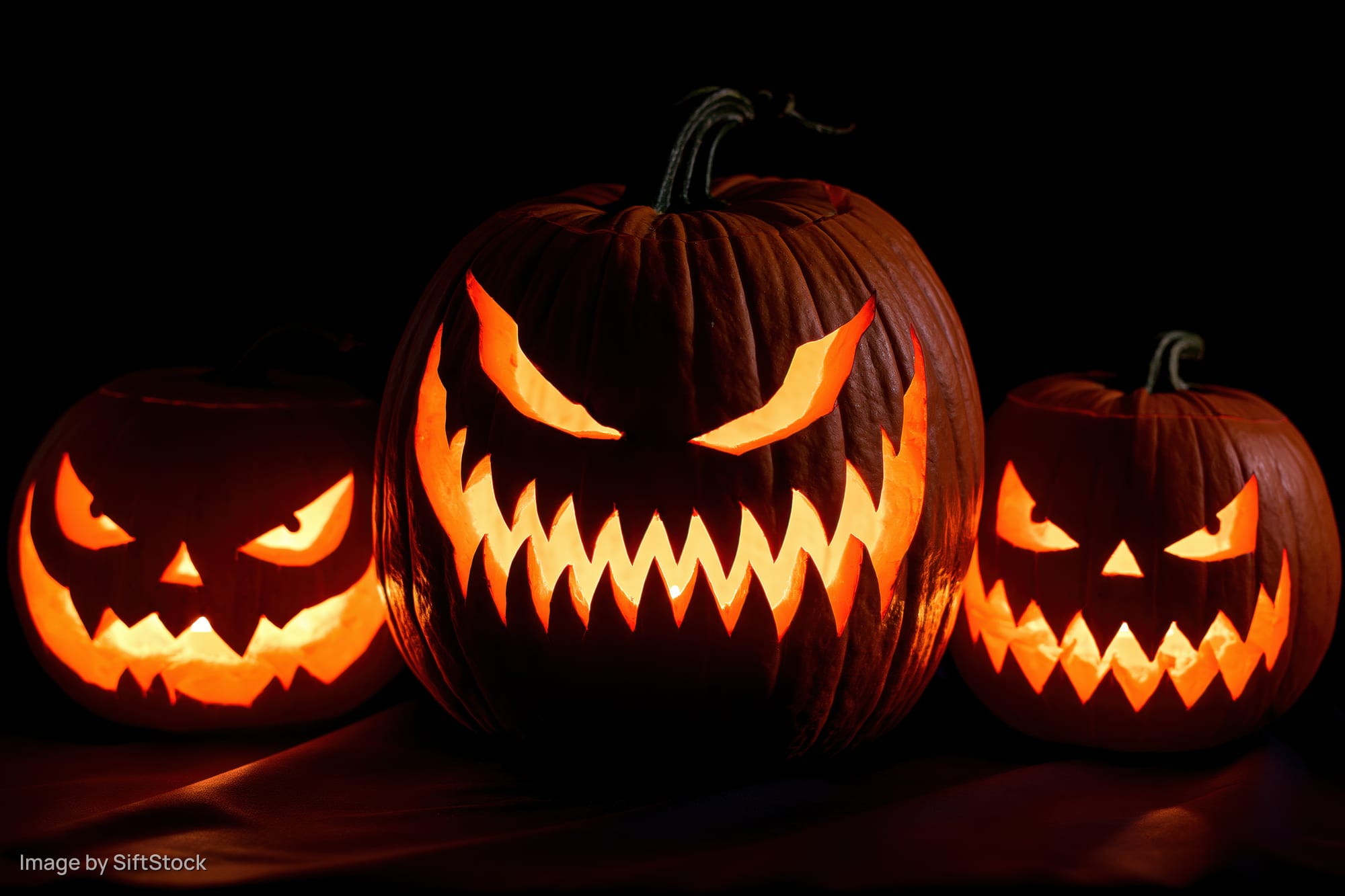 Three carved jack-o-lanterns glowing in the dark on a table