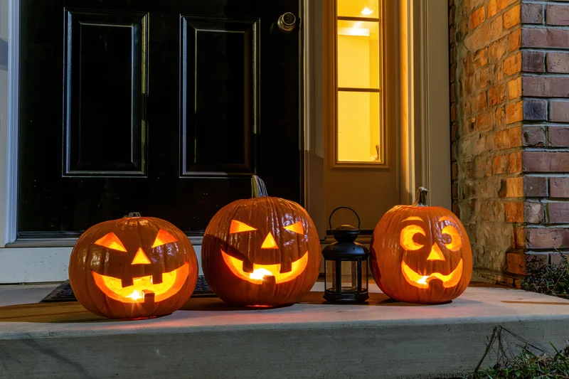 Three carved jack-o-lanterns glowing on a porch steps beside a door at night