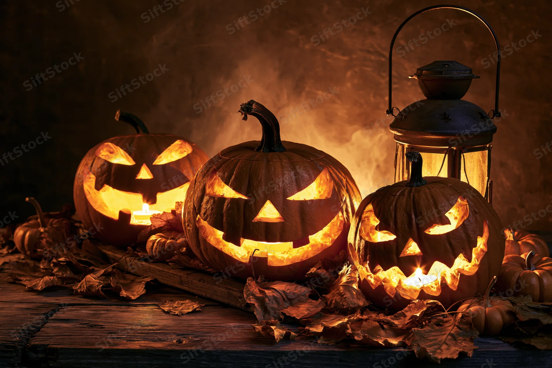 Three carved jack-o-lanterns glowing with candles on a wooden table surrounded by autumn leaves and a lantern