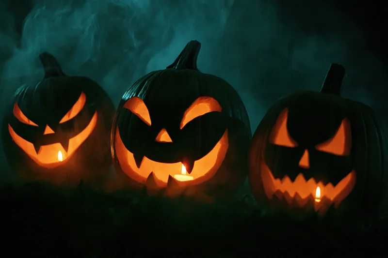 Three carved jack-o-lanterns glowing with candles in a smoky dark outdoor setting