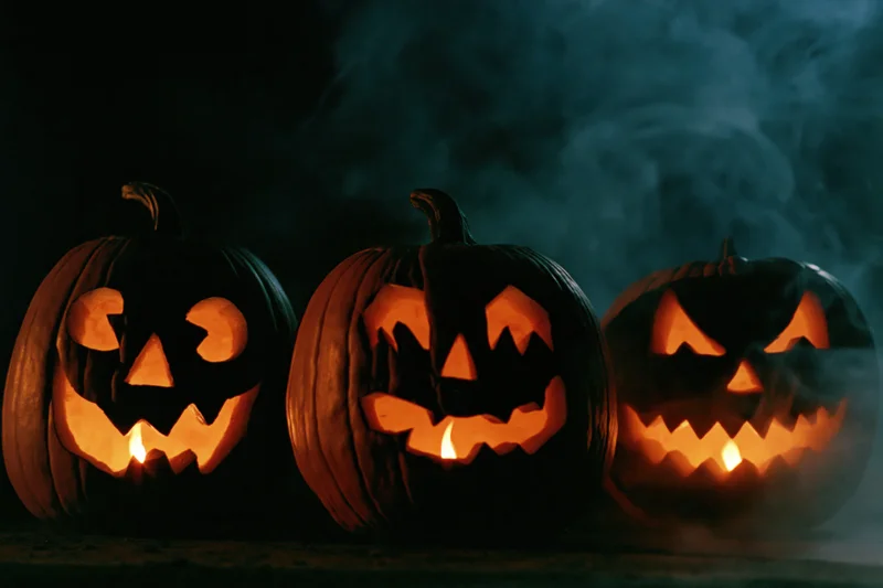 Three carved pumpkins glowing with candles in dark smoky setting