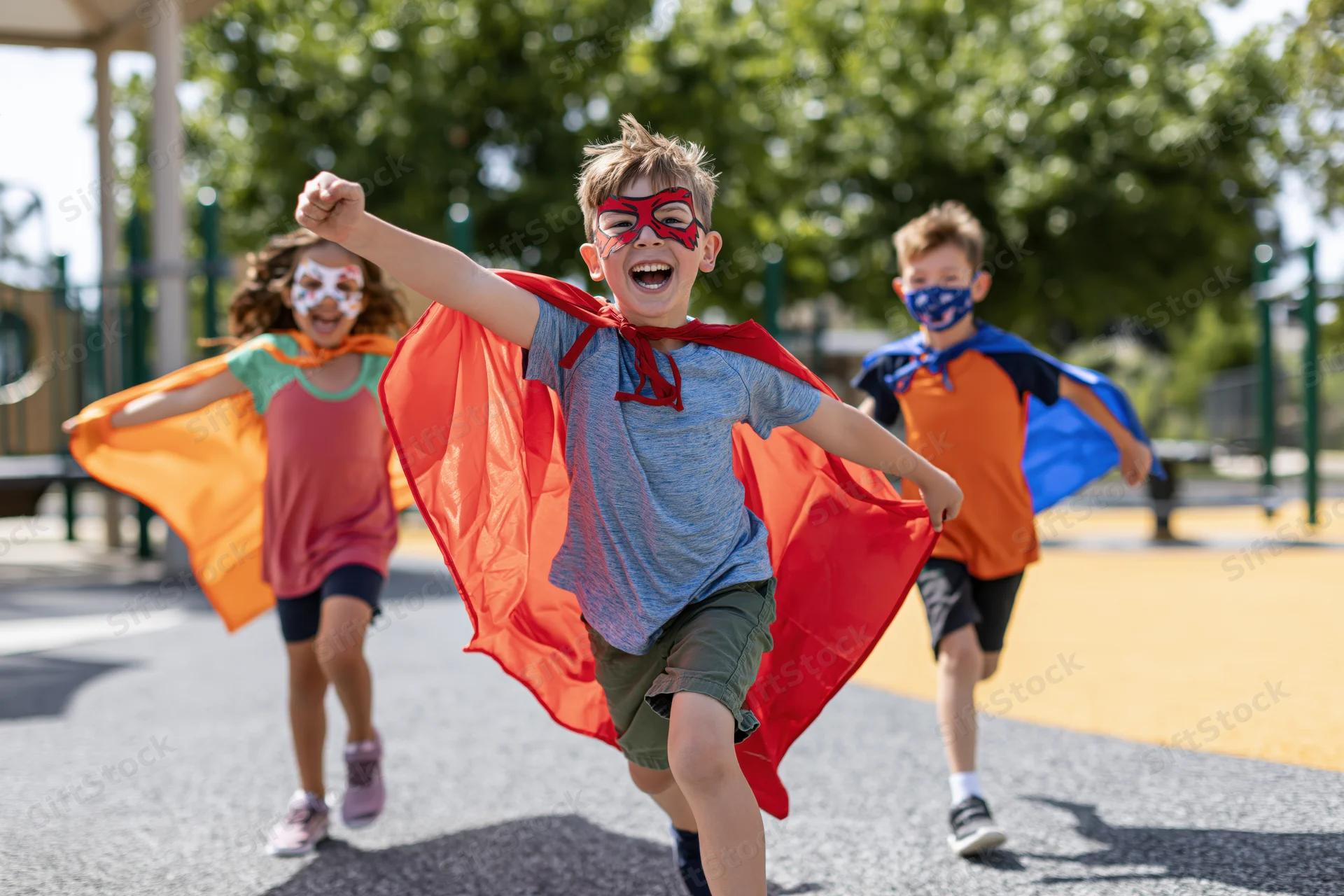 Three children in superhero costumes running toward camera on playground