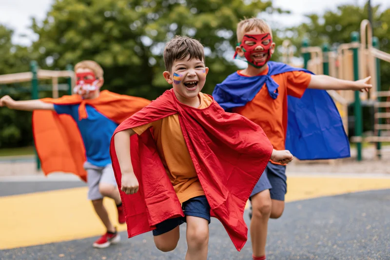 Three boys running toward camera in superhero costumes on playground