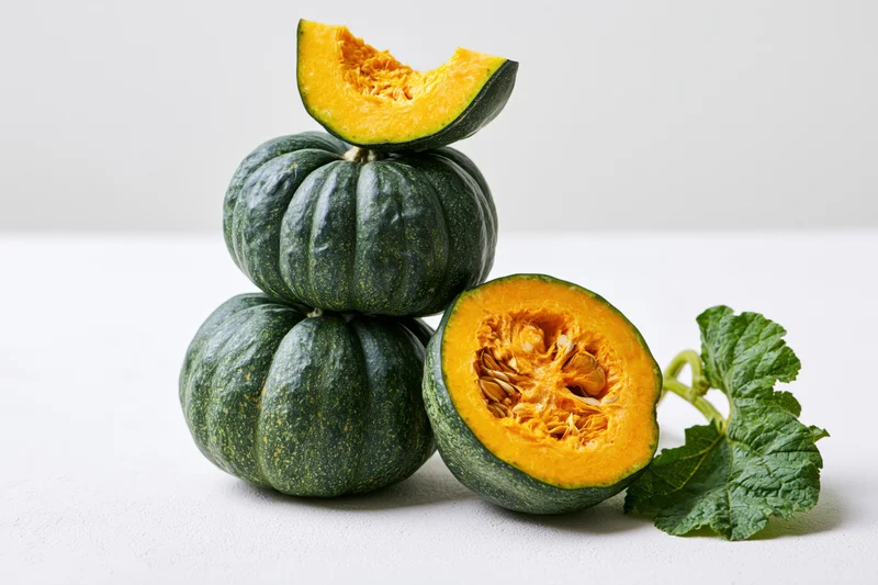 Stacked kabocha squash with cut halves and leaf on white surface