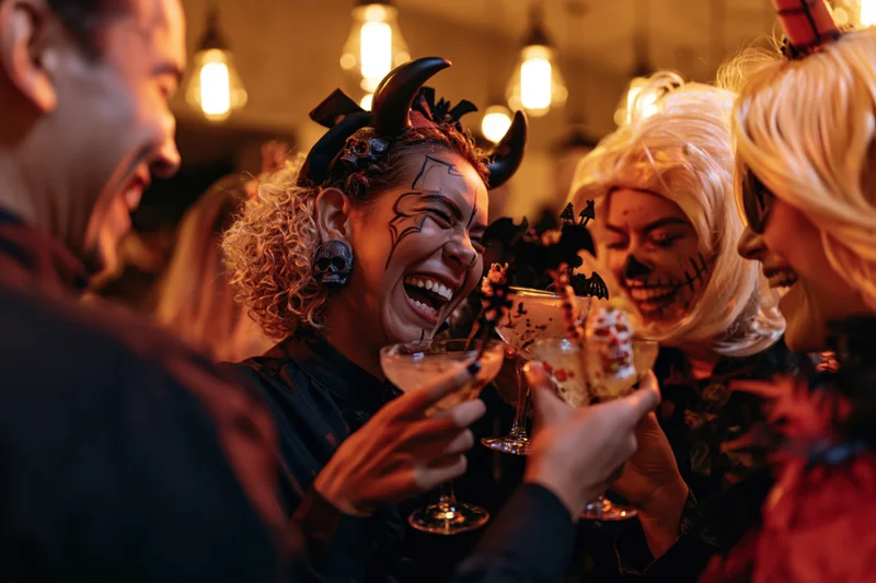 Friends in halloween costumes laughing and clinking cocktails at a bar party
