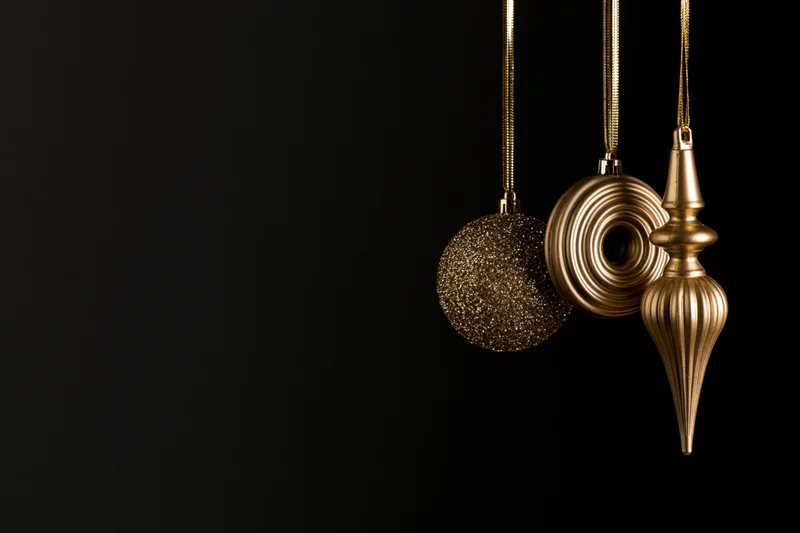 Three gold christmas ornaments hanging from ribbons against black background