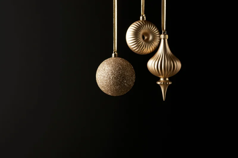 Three gold christmas ornaments hanging from ribbons against black background