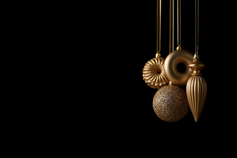Gold christmas ornaments hanging from ribbons against black background