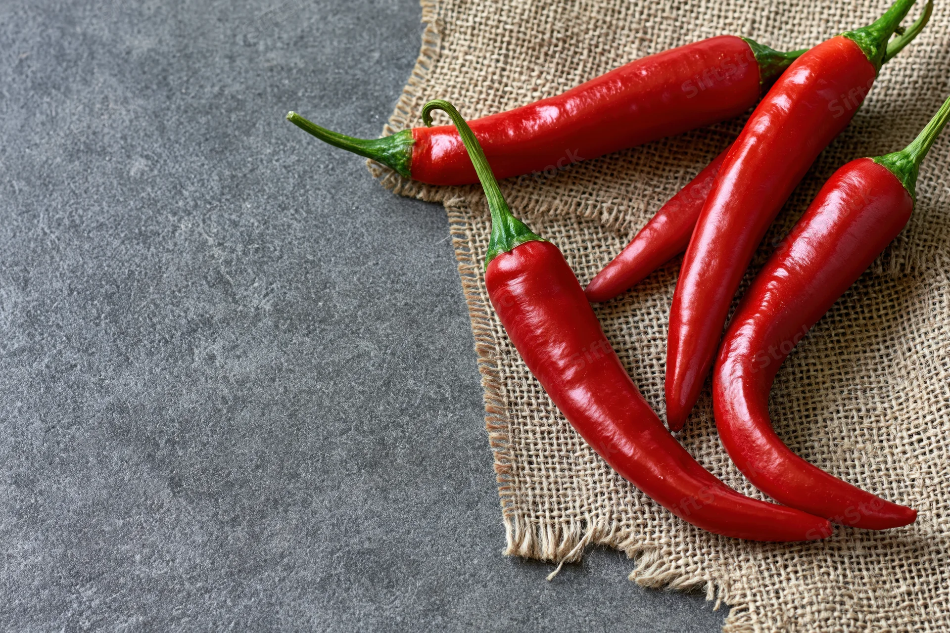 Red chili peppers resting on torn burlap cloth over gray stone surface