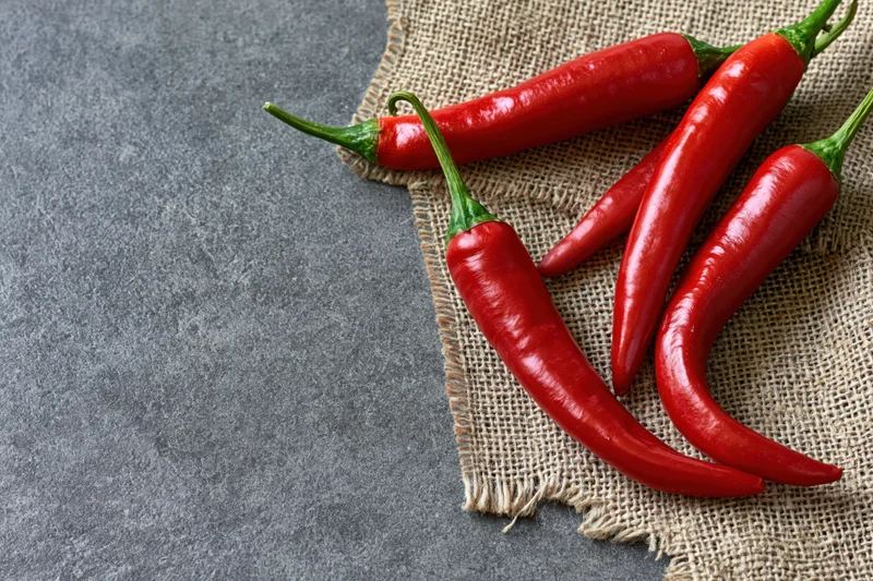 Red chili peppers resting on torn burlap cloth over gray stone surface