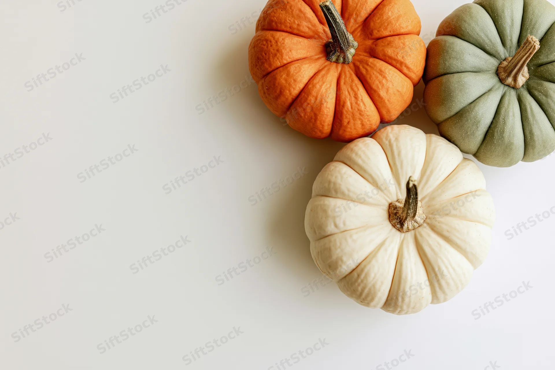 Three small decorative pumpkins arranged in the upper-right corner on a white surface