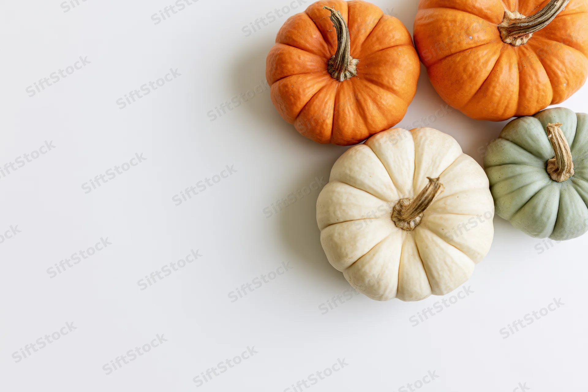 Four small decorative pumpkins in orange, white and green arranged in upper right corner on white surface