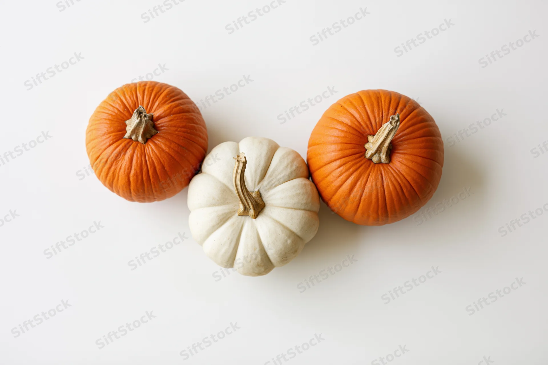 Three small decorative pumpkins arranged on a white surface in a flat lay composition