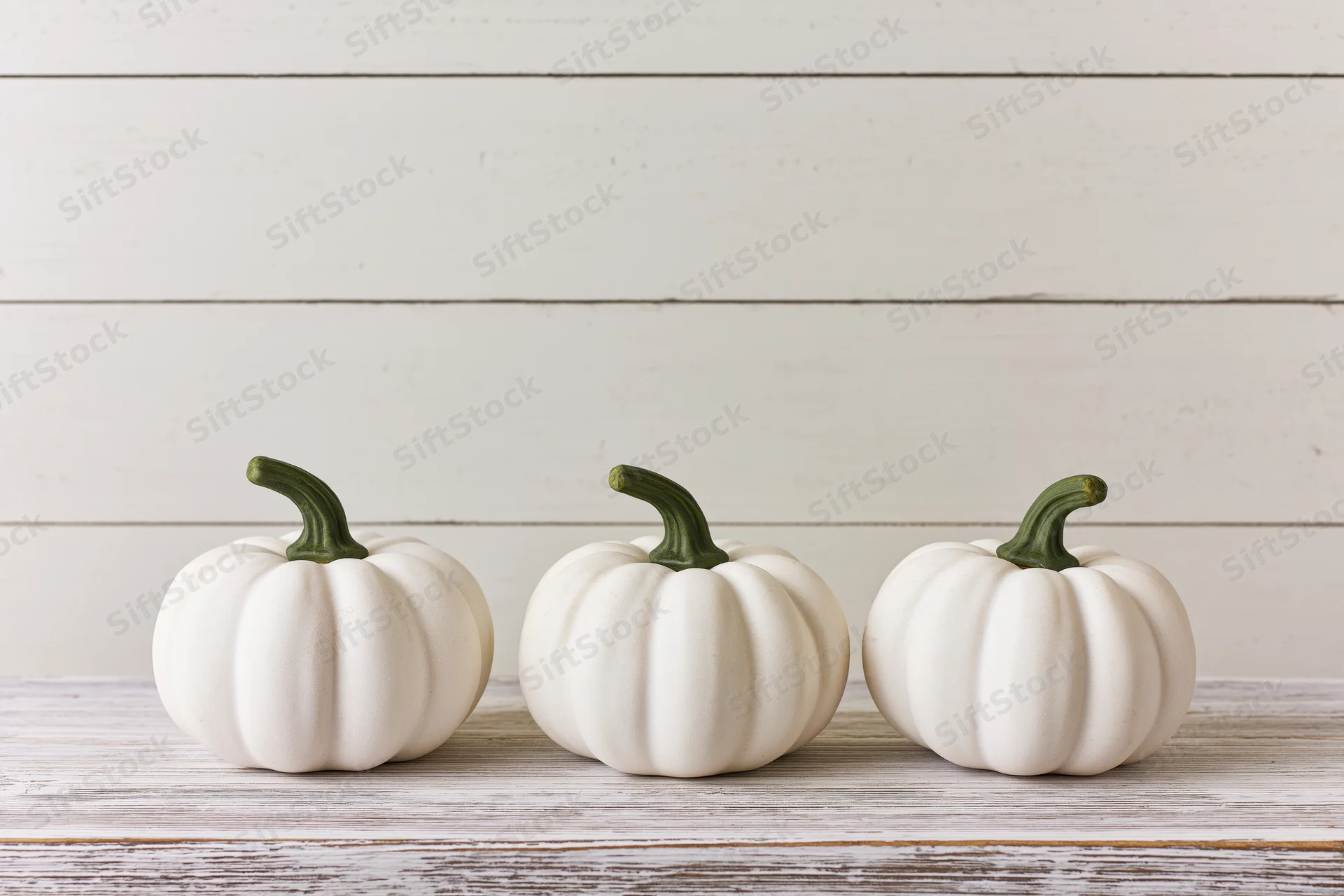 Three small white ceramic pumpkins with green stems arranged in a row on a wooden surface