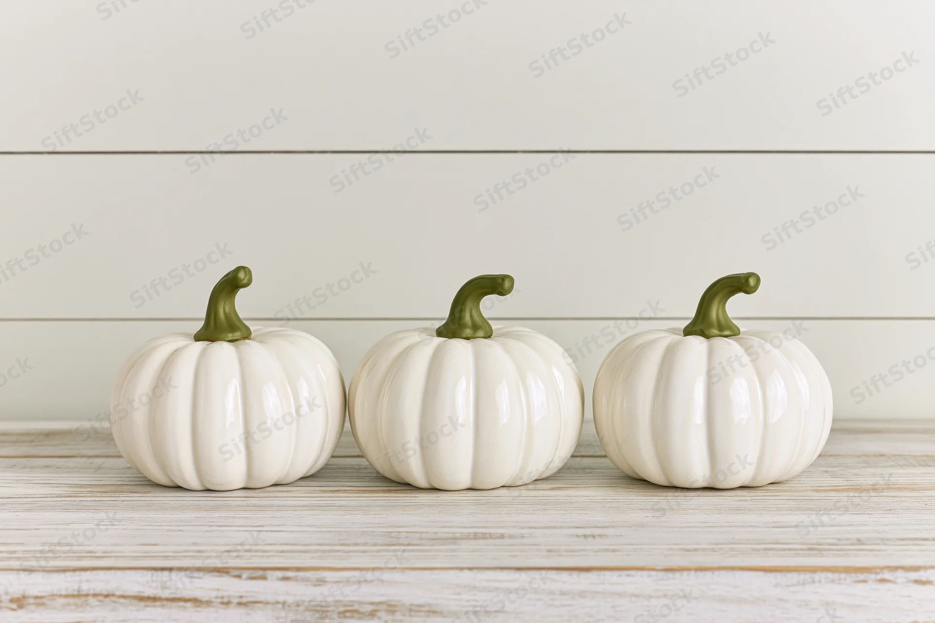Three white ceramic pumpkins arranged in a row on a wooden surface