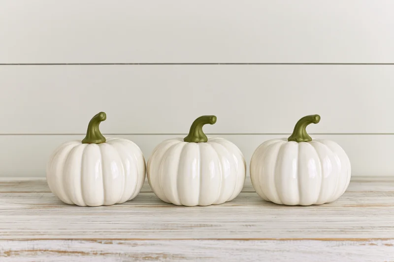 Three white ceramic pumpkins arranged in a row on a wooden surface