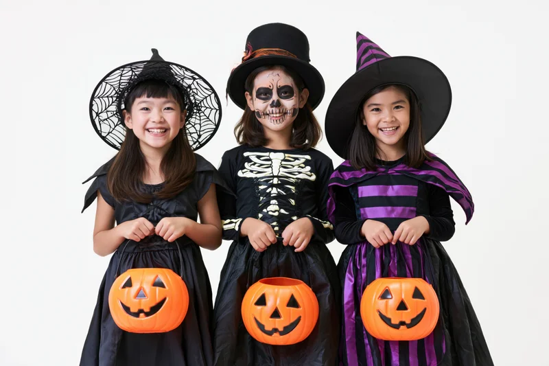 Three young asian girls in halloween costumes smiling while holding pumpkin buckets