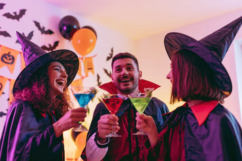 Three young adults in halloween costumes toasting with cocktails at a party