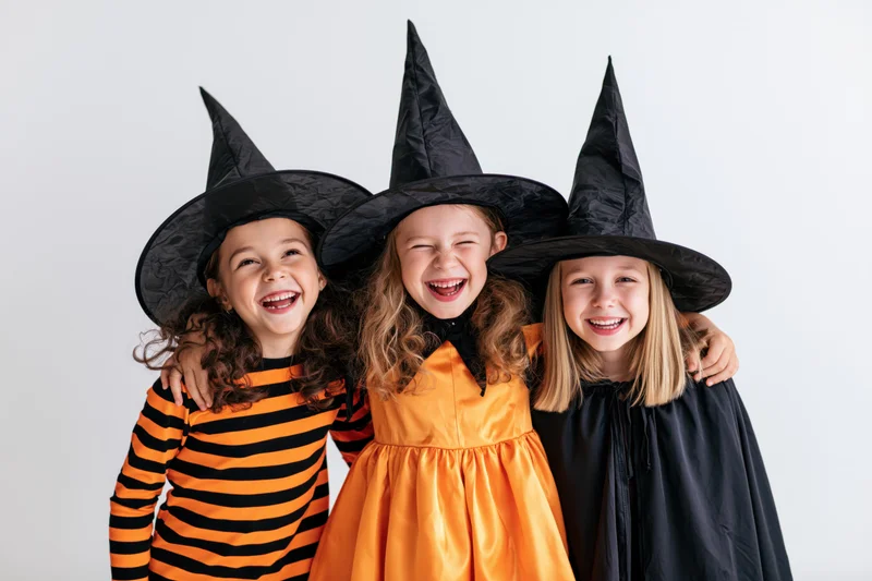 Three young girls in witch costumes laughing together in a studio setting