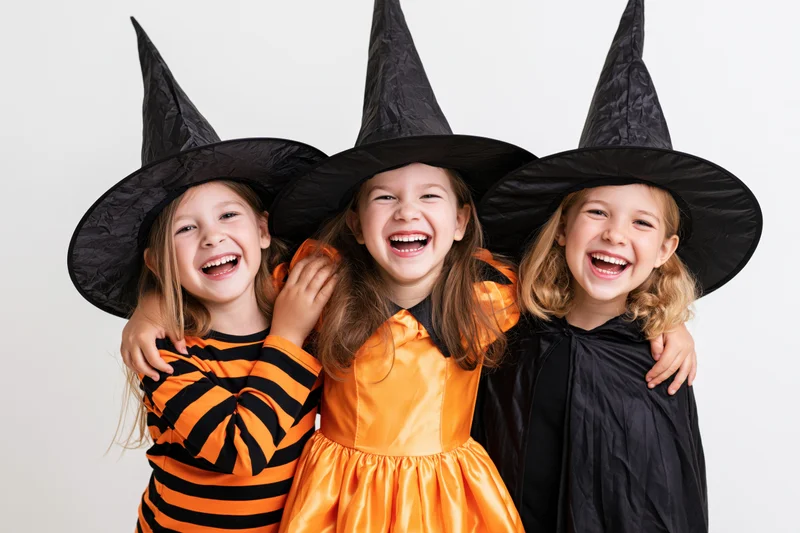 Three young girls in witch costumes laughing together in a studio setting