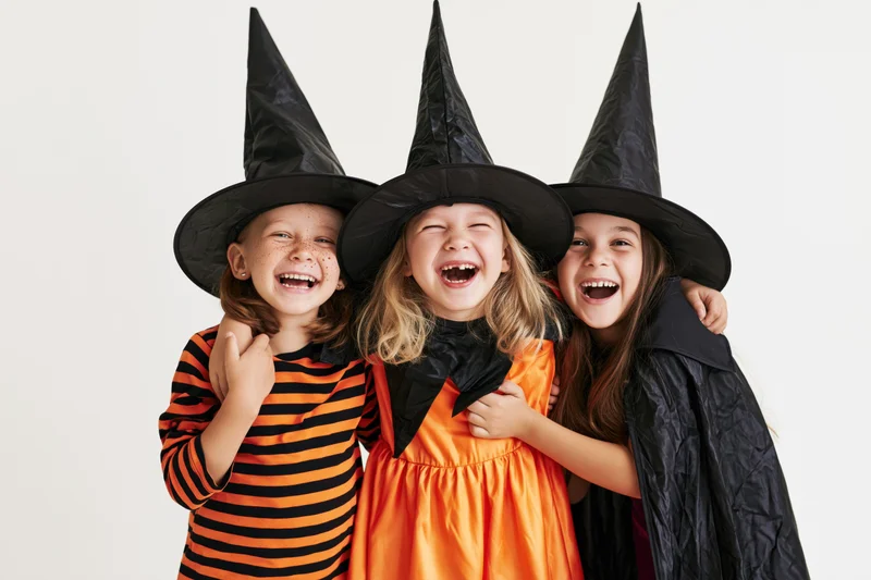 Three young children in witch costumes laughing together in a studio setting