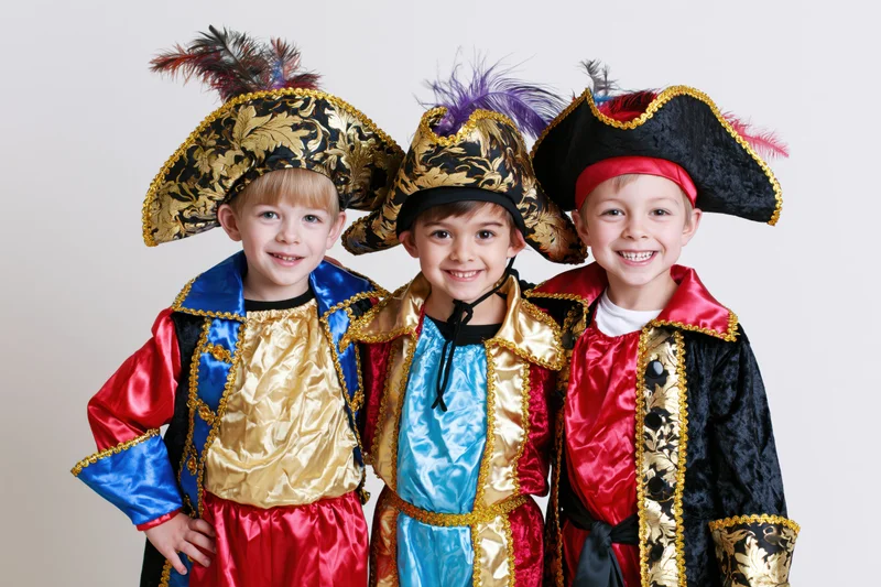 Three young boys in elaborate pirate costumes smiling together against a plain background