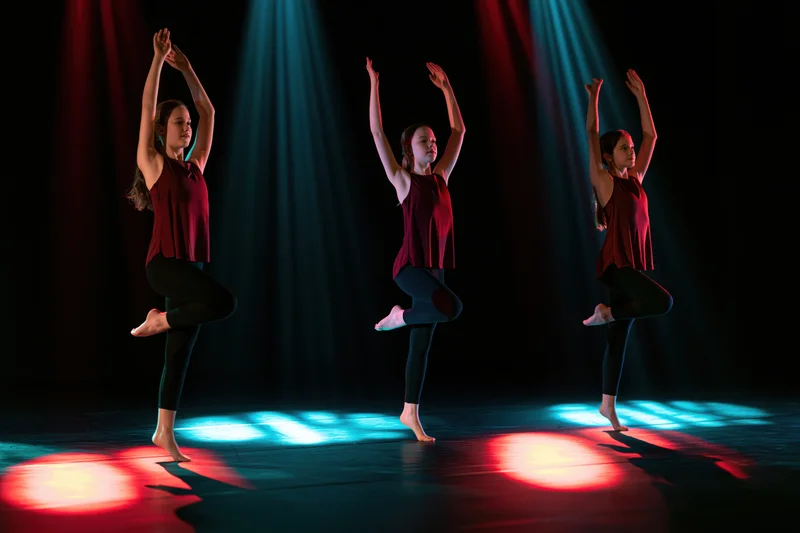 Three young girls performing synchronized contemporary dance on stage under colored spotlights