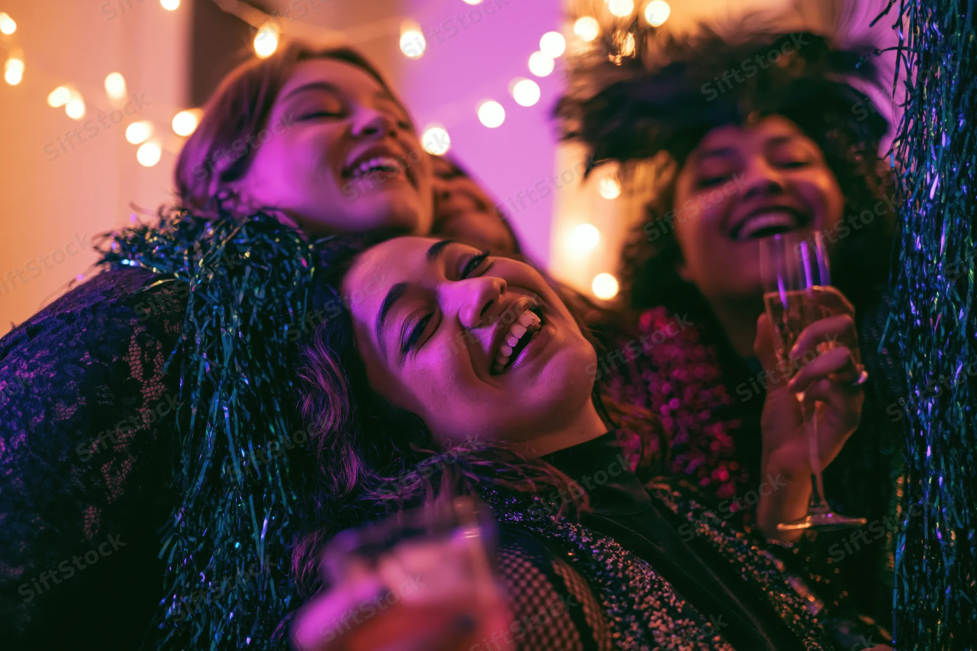 Three young women laughing and toasting with champagne at an indoor festive party