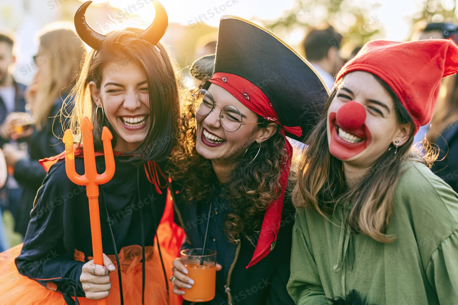 Three young women in halloween costumes laughing together outdoors at a party