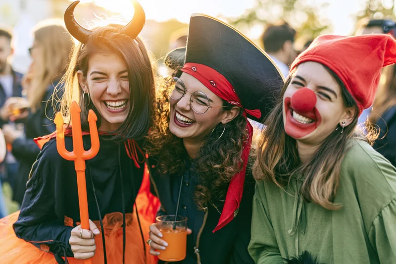 Three young women in halloween costumes laughing together outdoors at a party