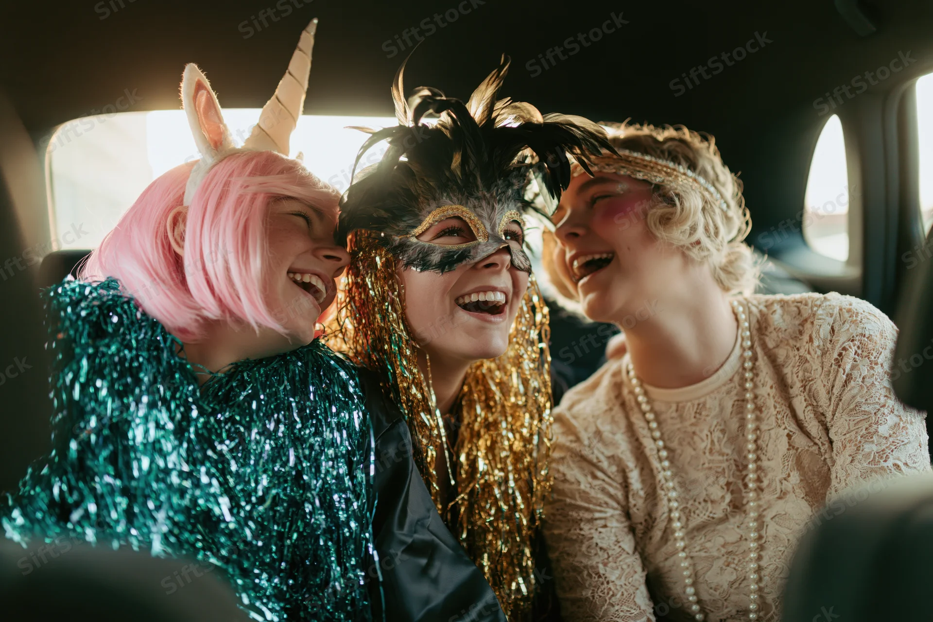 Three young women in party costumes laughing together in a car