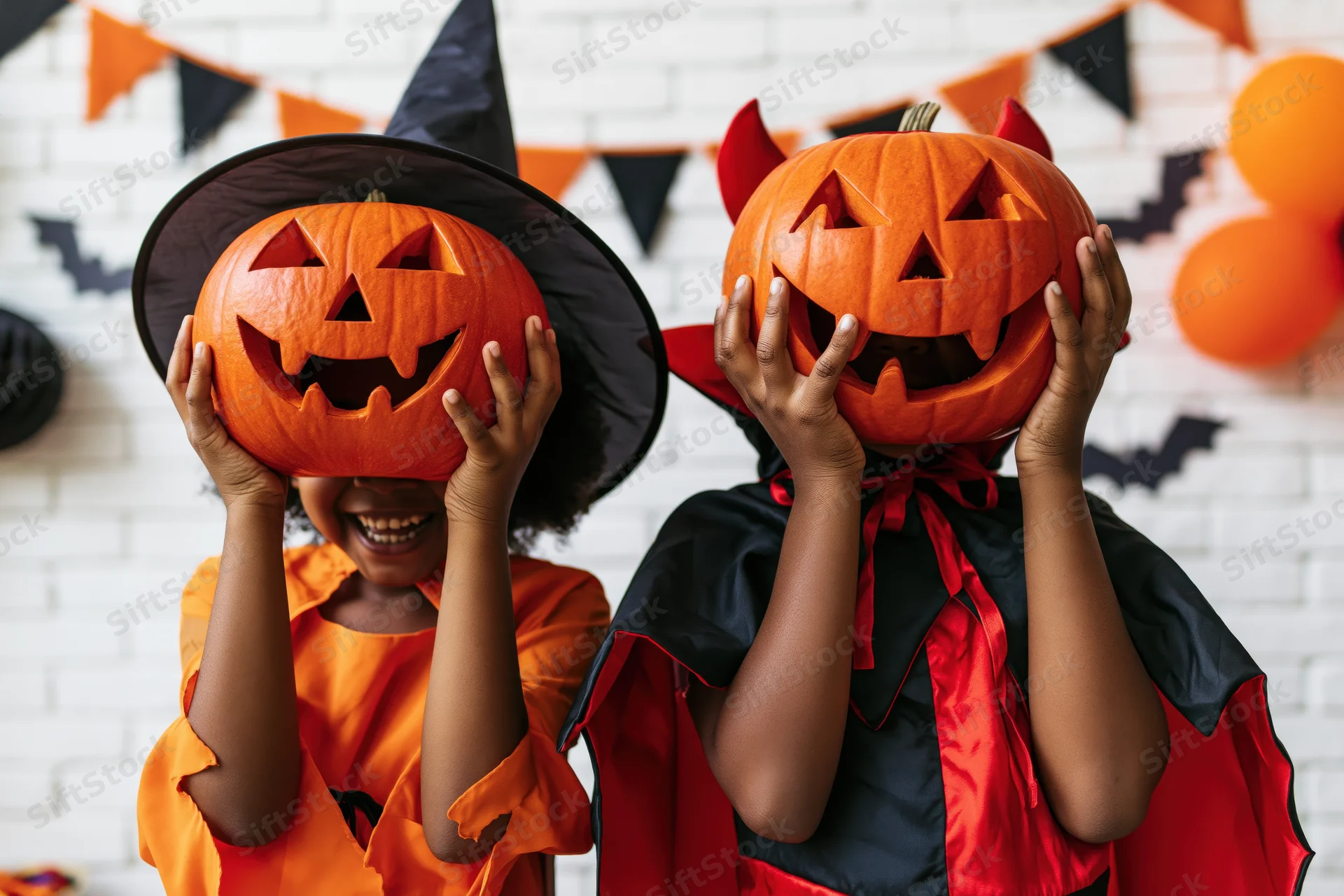 Two black children in halloween costumes holding carved pumpkins over their faces indoors