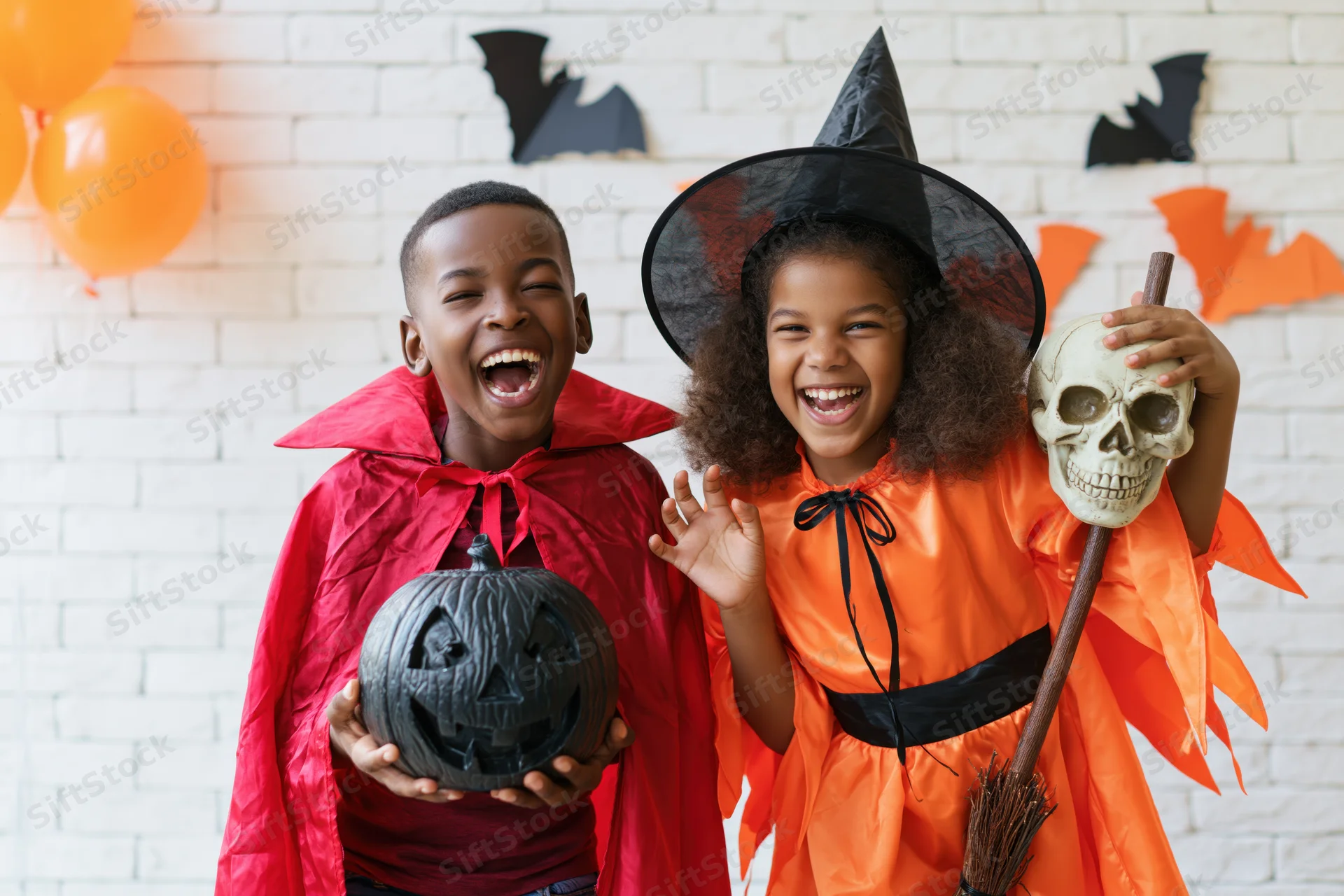 Two black children in halloween costumes laughing together in front of decorated brick wall