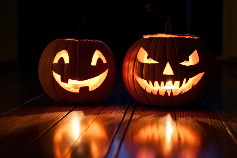 Two carved jack-o-lanterns glowing with candles on a dark wooden floor at night