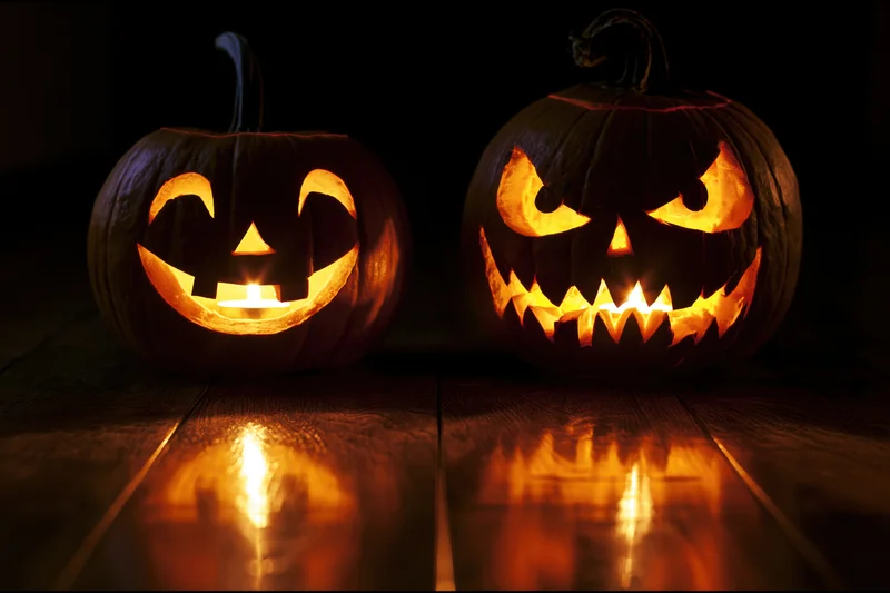 Two carved jack-o-lanterns glowing on a dark wooden floor with reflections
