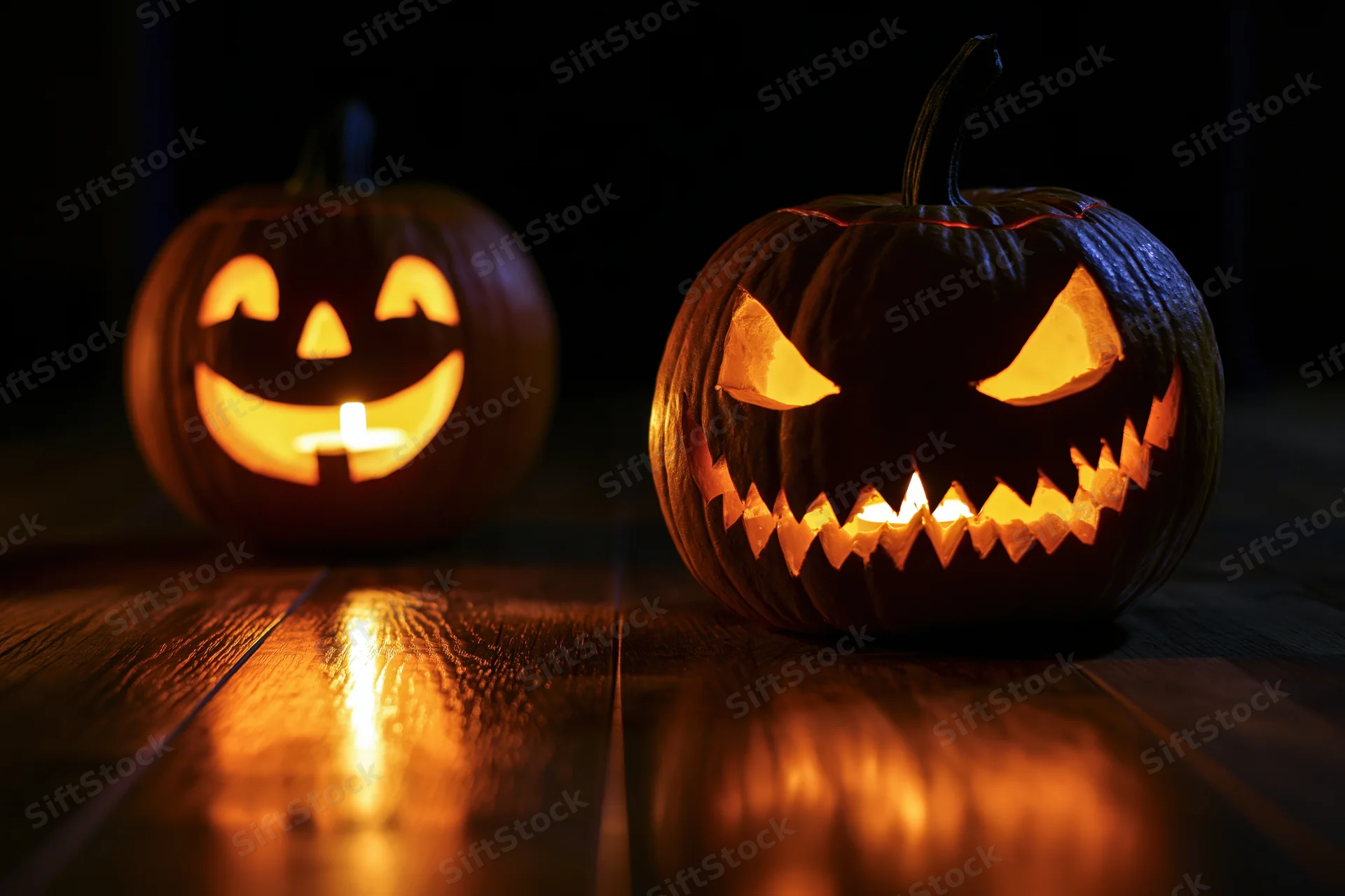 Two carved pumpkins with glowing faces on a dark wooden floor at night