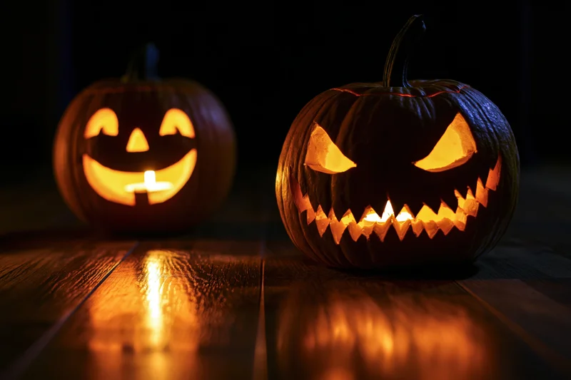 Two carved pumpkins with glowing faces on a dark wooden floor at night