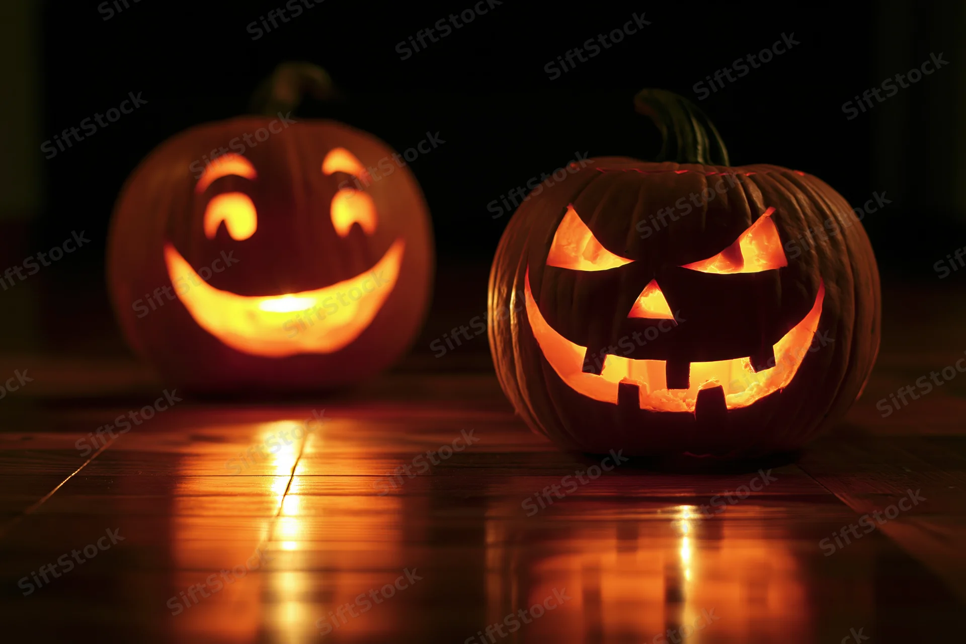 Two carved pumpkins glowing with light on a dark wooden floor