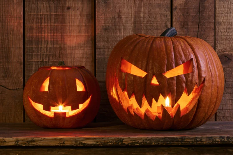Two carved pumpkins with glowing candles on a wooden shelf