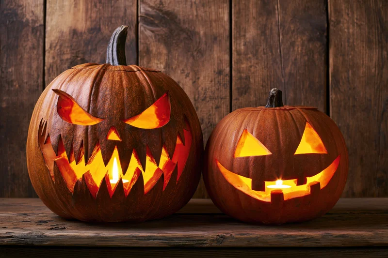 Two carved pumpkins with glowing candles on a wooden table