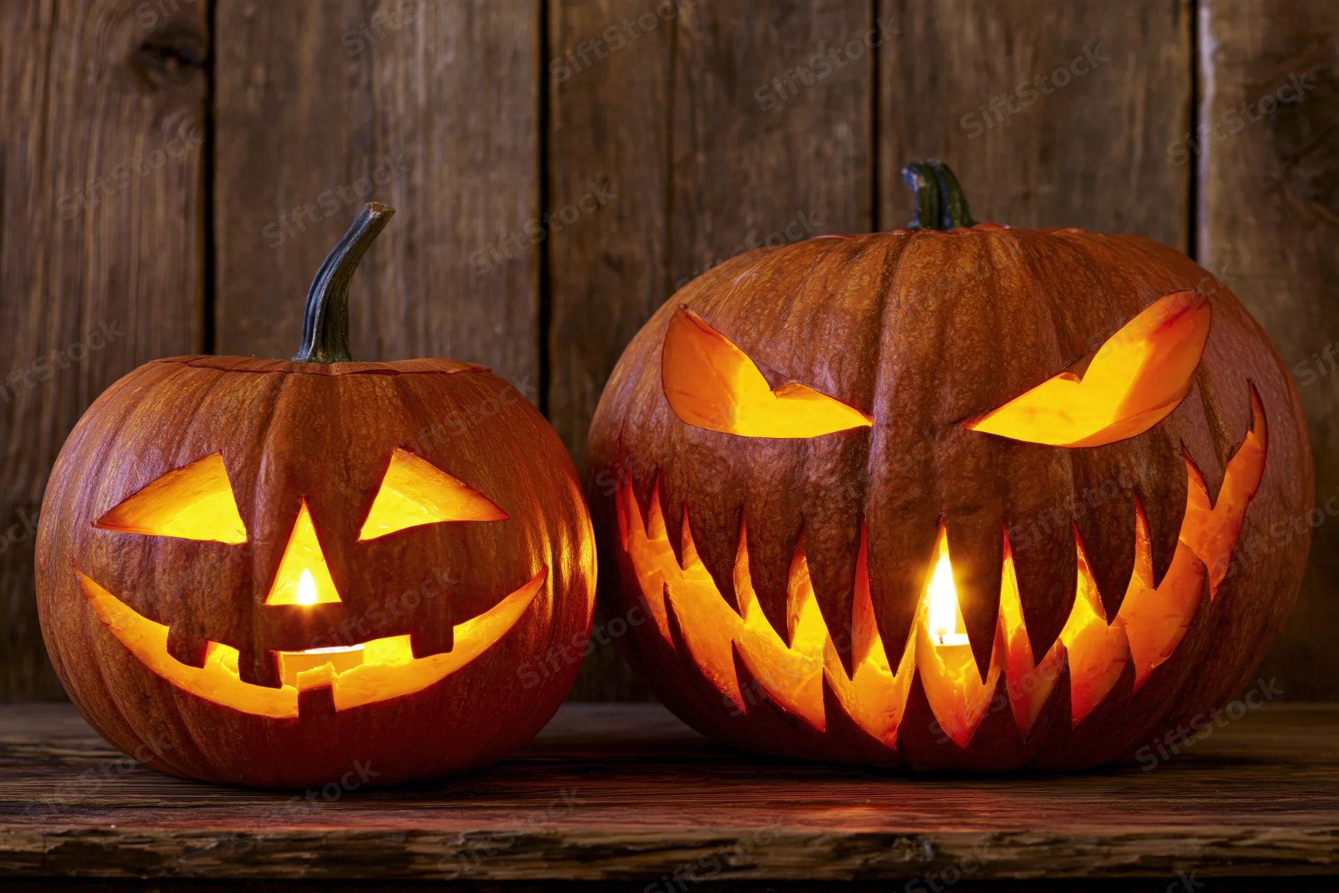 Two carved pumpkins glowing with candles on a wooden surface