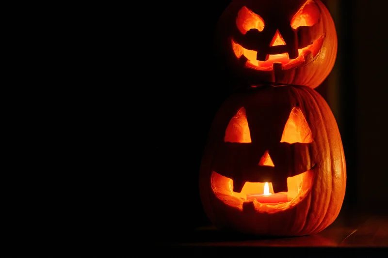 Two carved jack-o-lanterns stacked with candles glowing in the dark