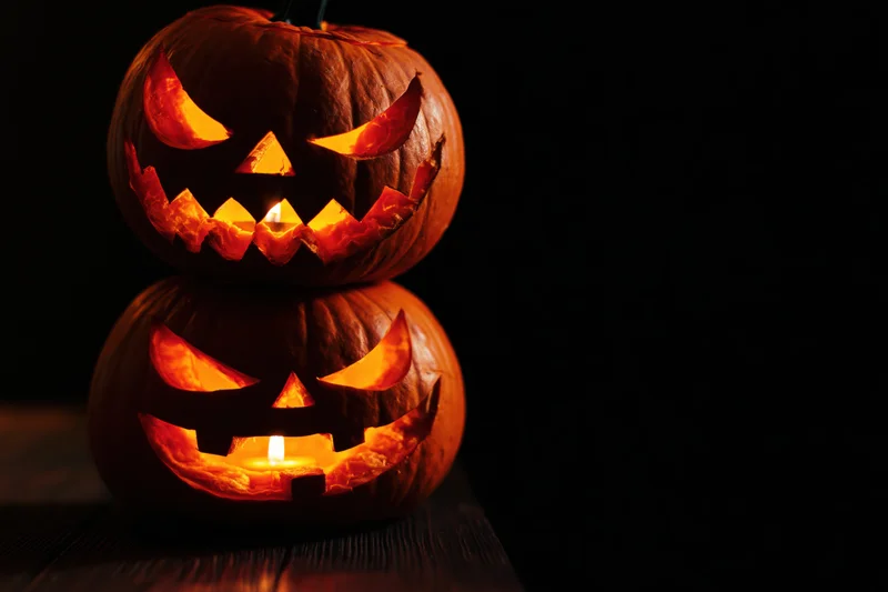 Two carved jack-o-lanterns stacked with candles glowing in the dark on a wooden surface