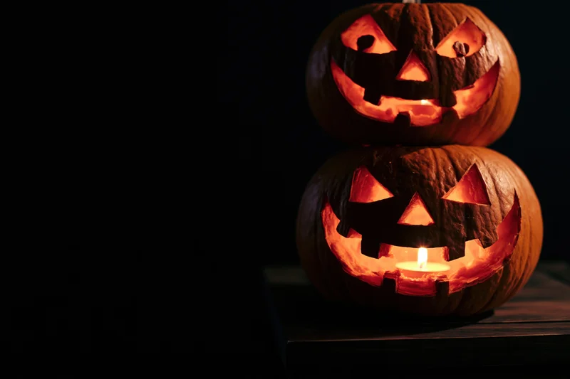 Two carved jack-o-lanterns stacked on a wooden table glowing with candlelight in the dark