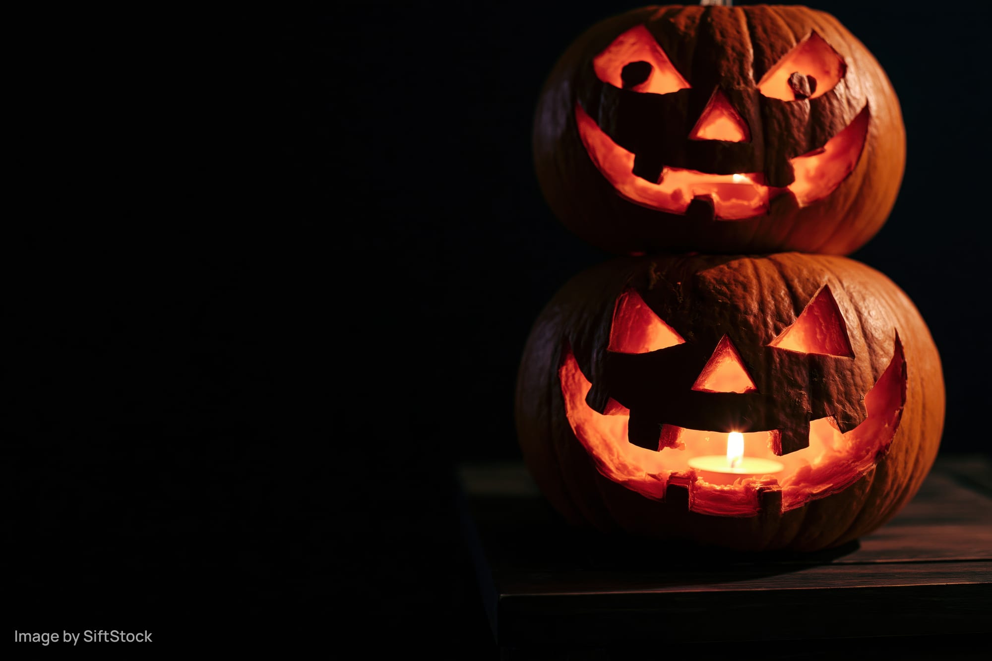 Two carved jack-o-lanterns stacked on a wooden table glowing with candlelight in the dark