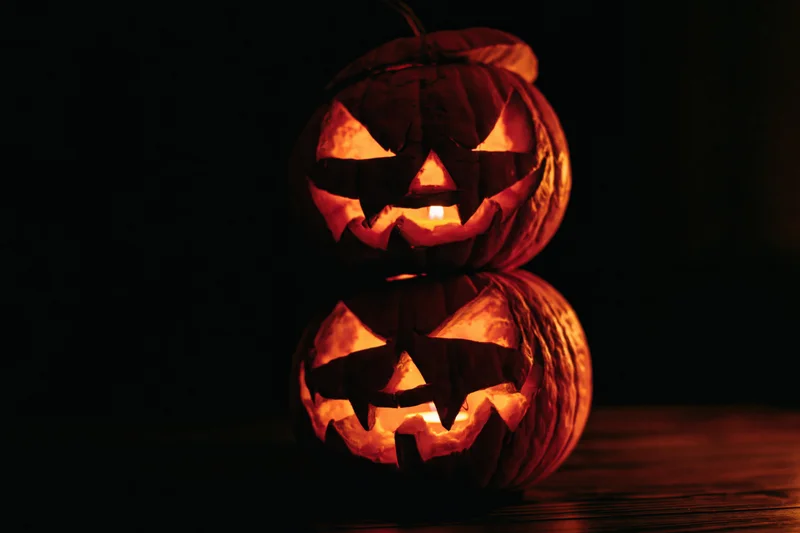 Two carved jack-o-lanterns stacked and glowing with candles on a dark wooden surface