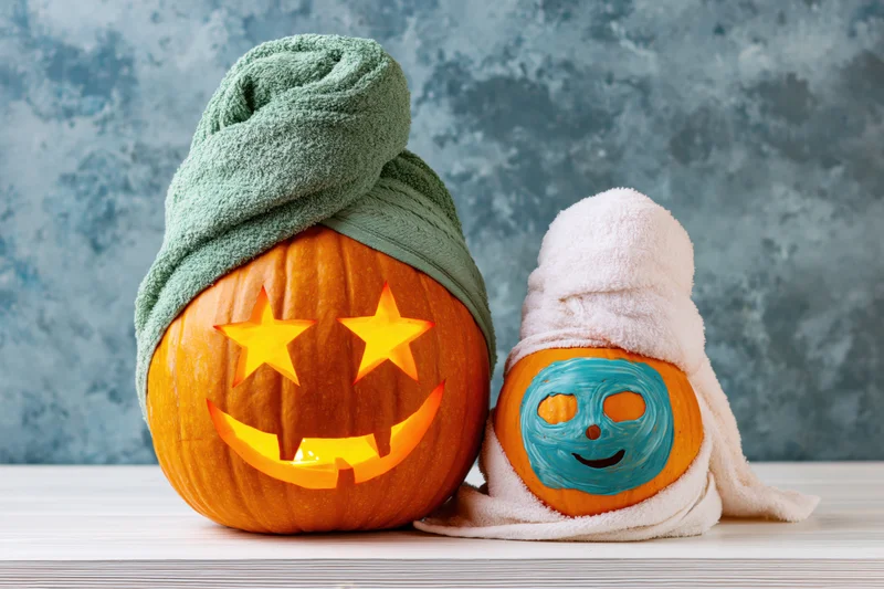 Two carved halloween pumpkins styled as spa characters with towels on a wooden table