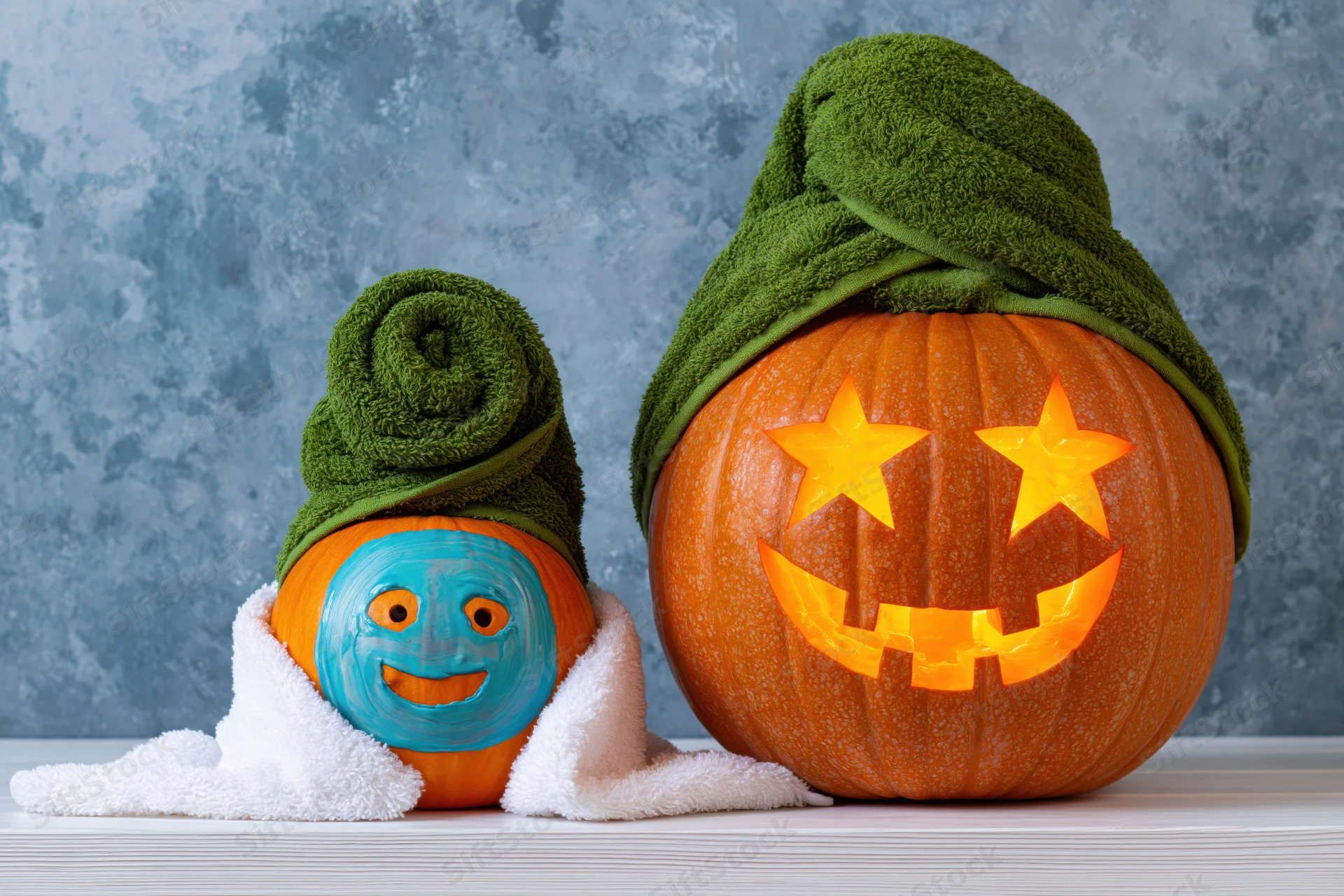 Two carved pumpkins styled as spa characters with towels and painted faces on a table