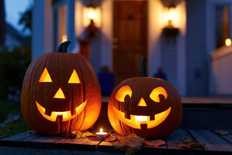 Two carved jack-o-lanterns glowing on a wooden front porch at evening